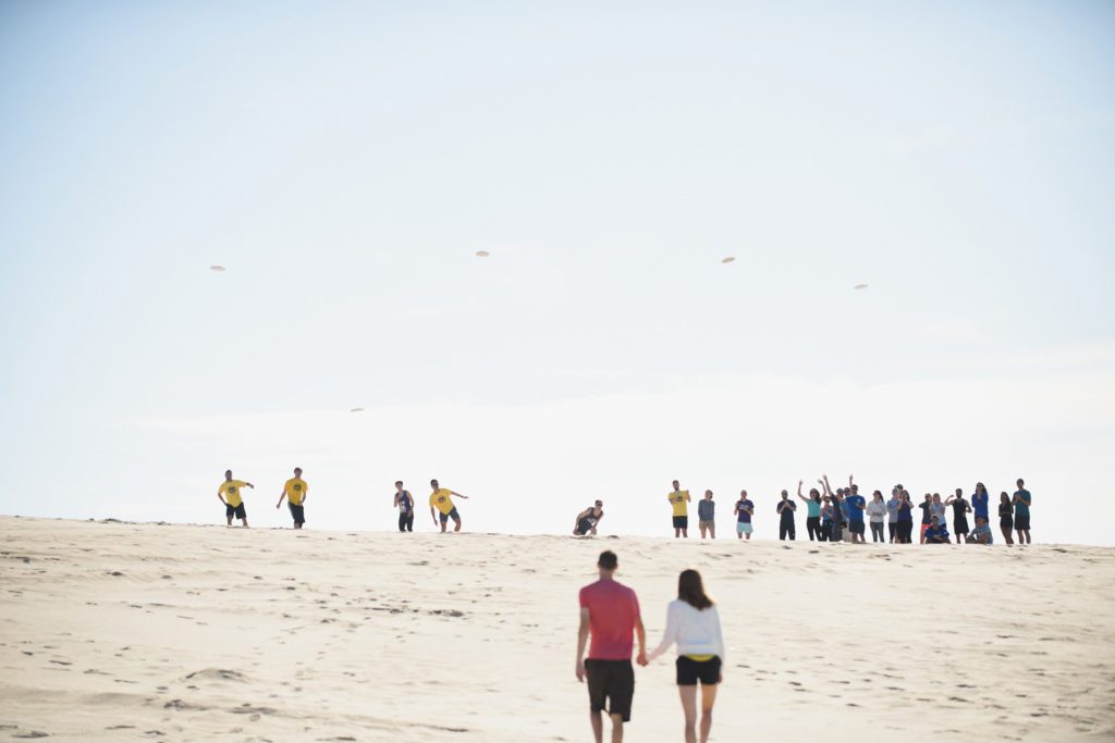 Friends throw frisbees to engaged couple at Jockey's Ridge