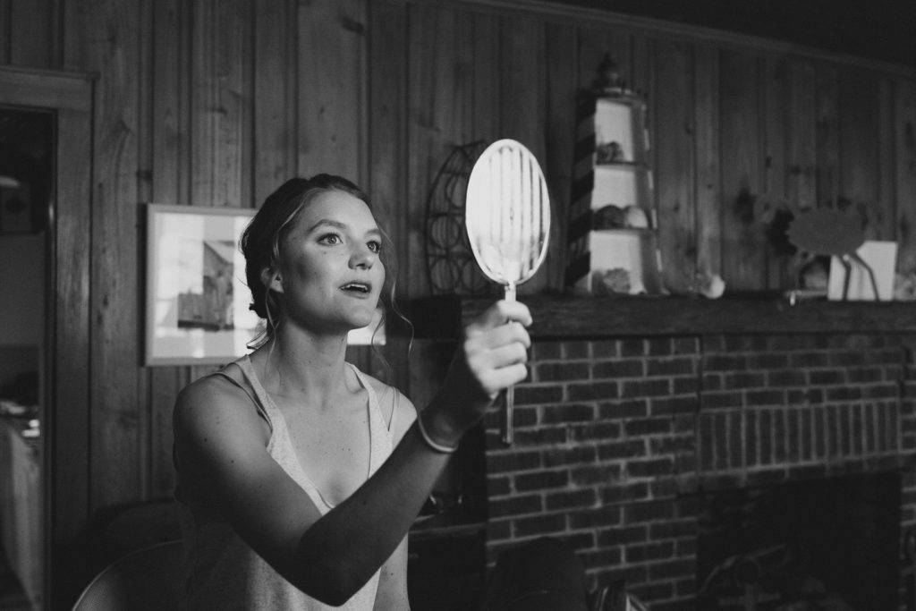 Bride looks in mirror during hair and makeup for her Outer Banks wedding