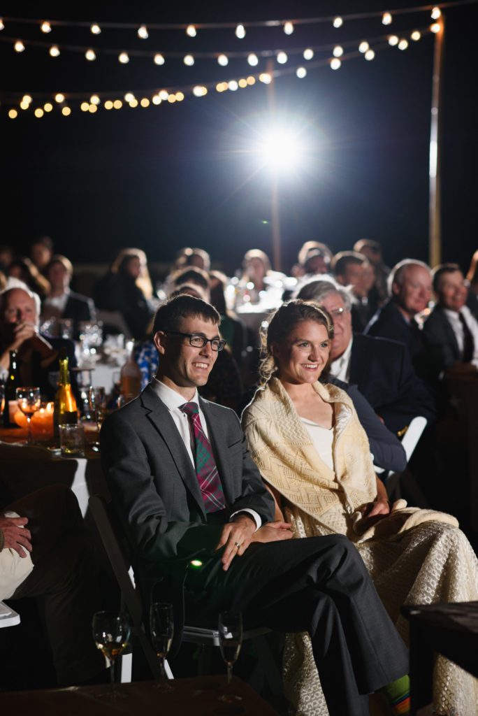 Bride and groom sitting with guests during wedding toasts
